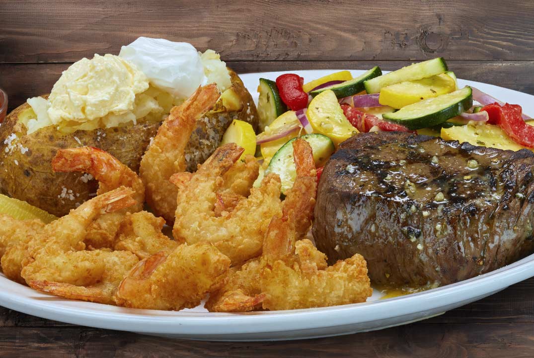 a plate of sirloin steak, shrimp with potatoes and veggies