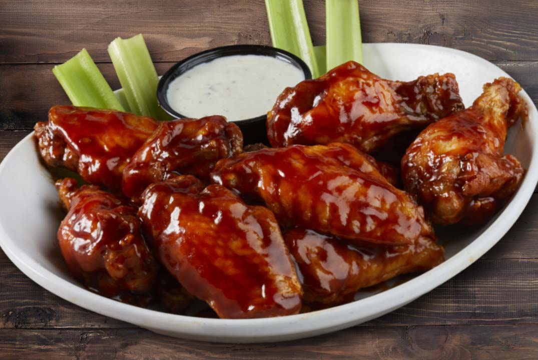 a plate of chicken wings tossed in sauce with celery an dipping sauce