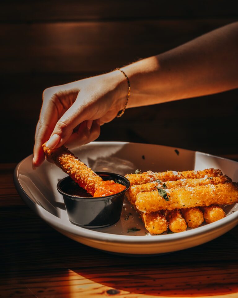 Mozzarella Stick being dipped in marinara sauce with a stack of mozzarella sticks next to it